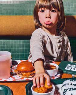 Enfant devant un burger et des frites dans un restaurant bio, avec des éléments de restauration familiale.
