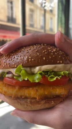 Un burger dans une main, avec du pain au sésame, de la laitue, des tomates et une sauce crémeuse.