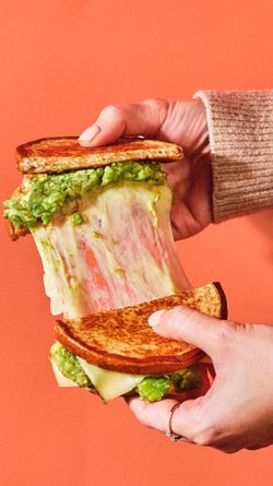 Un sandwich avec du fromage fondu, du pain grillé et de l'avocat, au sein d'un décor orange.