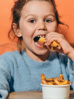 Enfant mangeant des frites dans un restaurant burger bio adapté aux enfants, ambiance chaleureuse et conviviale.