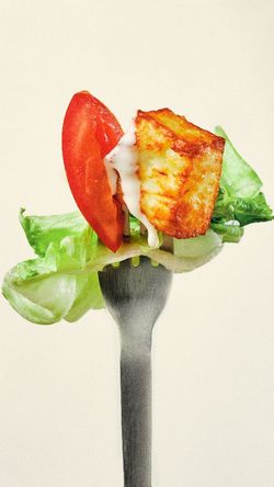 Une fourchette tenue avec une feuille de laitue, une tranche de tomate, un morceau de fromage grillé et une olive.