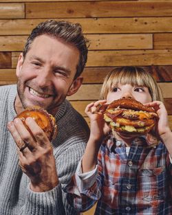 Un adulte et un enfant tenant chacun un burger, assis devant un mur en bois, dans un restaurant burger bio et kids friendly