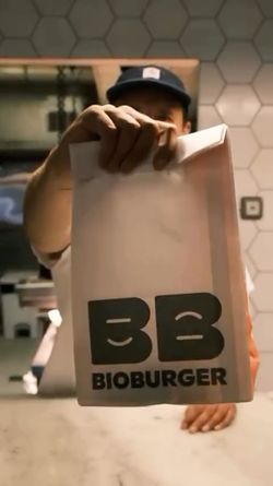 Un employé tenant un sac à emporter avec le logo Bioburger dans un restaurant à l'ambiance moderne.