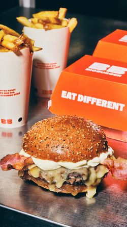 Un burger bio garni de bacon et fromage, accompagné de frites, dans un cadre convivial.