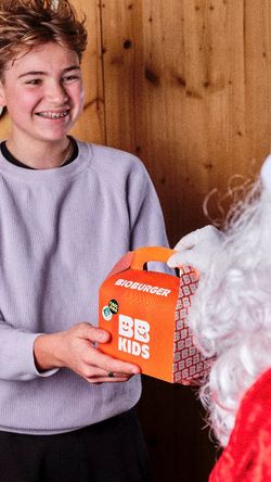 Une enfant heureux tient une boîte orange de burger bio pour enfants devant un personnage en costume.
