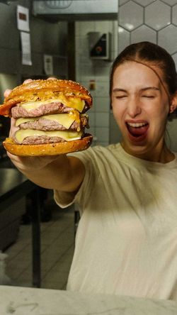 Burger biologique avec plusieurs steaks et du fromage, présenté par une personne souriante.