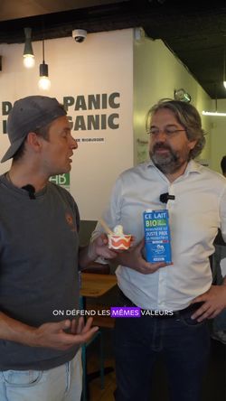 Deux personnes dans un restaurant bio discutant avec un produit laitier biologique à la main, intérieur simple et chaleureux.
