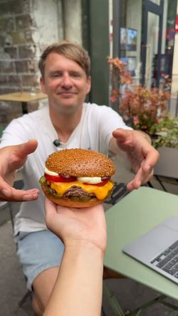 Restaurant burger bio à Toulouse proposant un burger avec fromage cheddar, tomates, et sauce blanche sur terrasse extérieure.