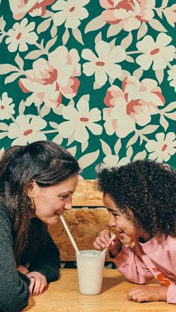 Moment complice entre une mère et sa fille partageant un milkshake dans un cadre convivial.