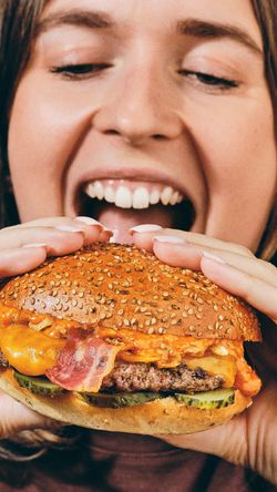 Personne tenant un gros burger bio avec du bacon, fromage et cornichons au restaurant Bioburger Rosa Parks.