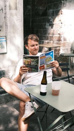 Homme assis dehors lisant un menu dans un restaurant burger bio avec bouteille et gobelet sur la table verte.