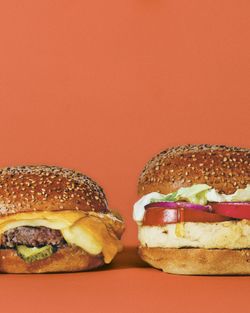 Deux burgers bio côte à côte, l'un avec fromage fondu et cornichons, l'autre avec légumes frais sur un fond orange.