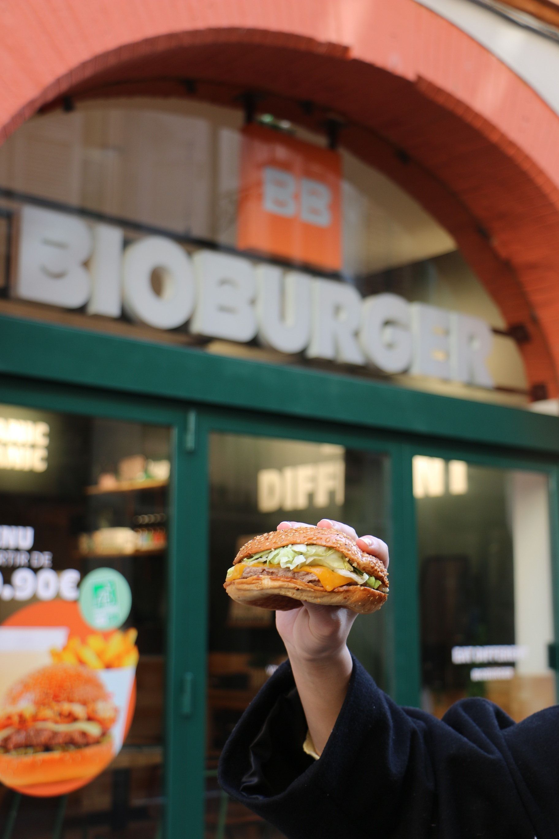 Restaurant bio Bioburger Toulouse Carmes avec un burger tenu devant la vitrine affichant le nom de l'établissement.