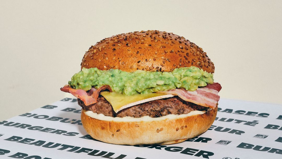 Burger bio garnie de viande, fromage, bacon et une couche de guacamole sur un pain au sésame.