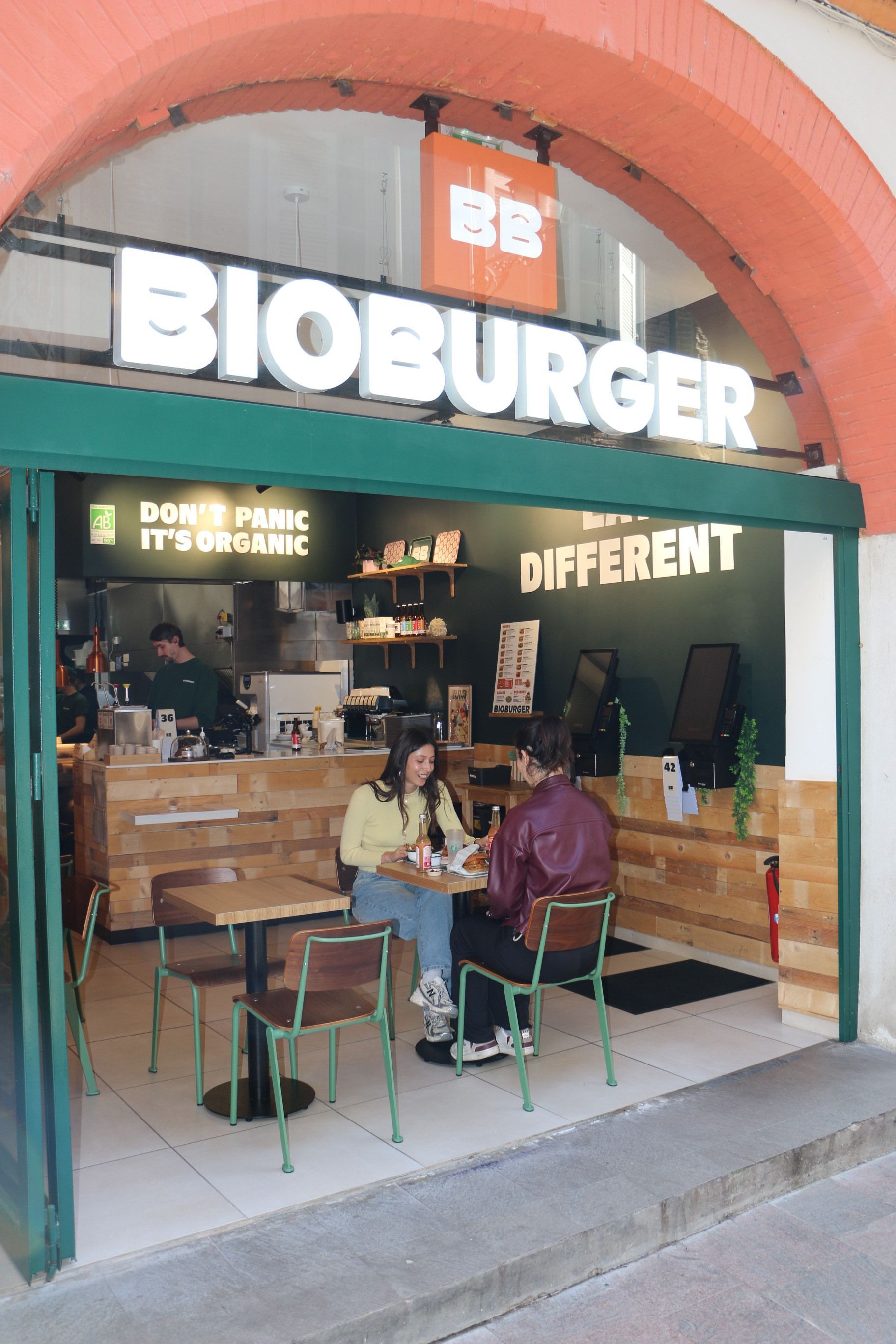 Façade du Bioburger Toulouse Carmes avec enseigne lumineuse, tables en bois, et clients à l'intérieur du restaurant bio.