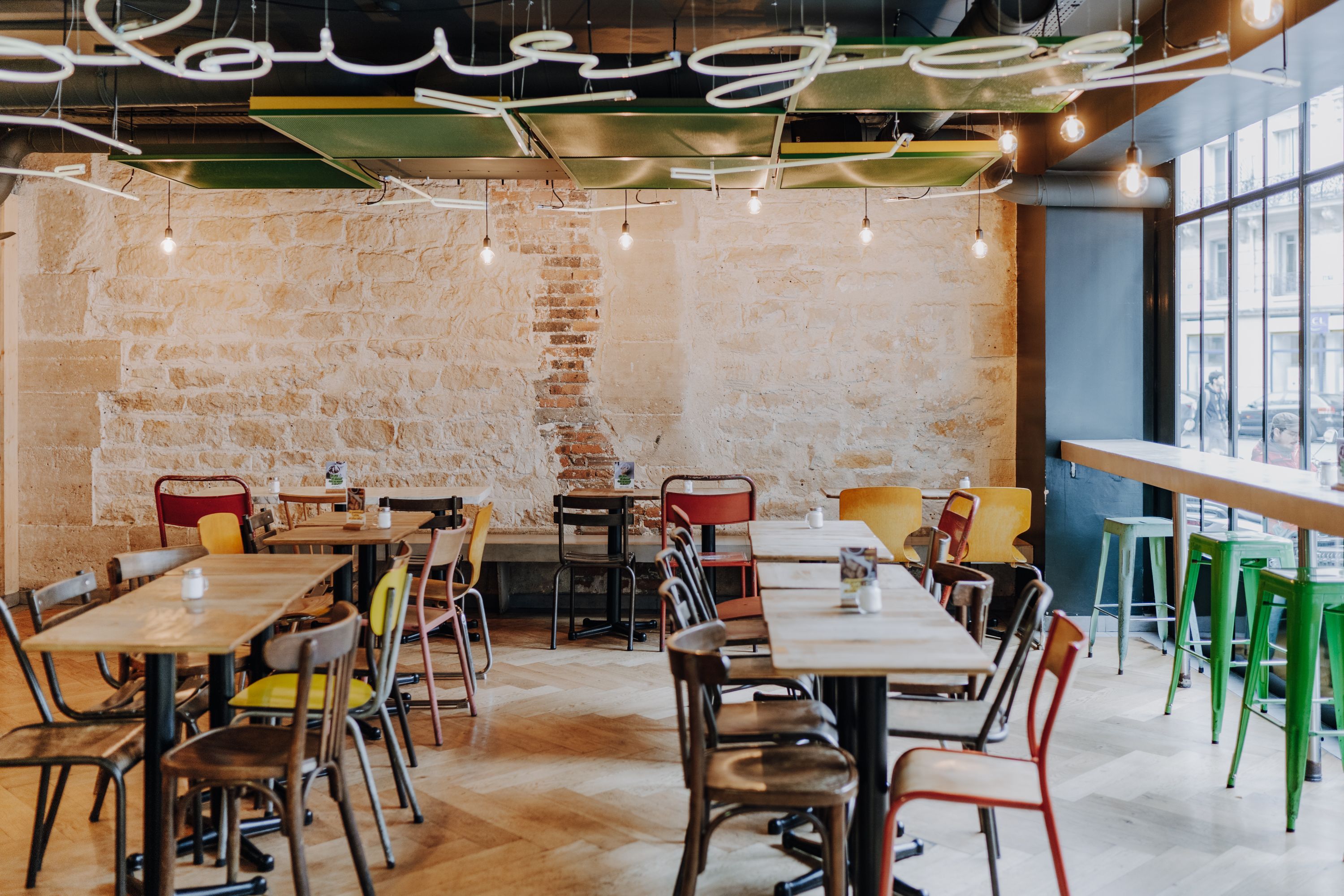 Ambiance moderne du restaurant avec tables en bois et chaises colorées. Espace convivial et adapté aux repas.