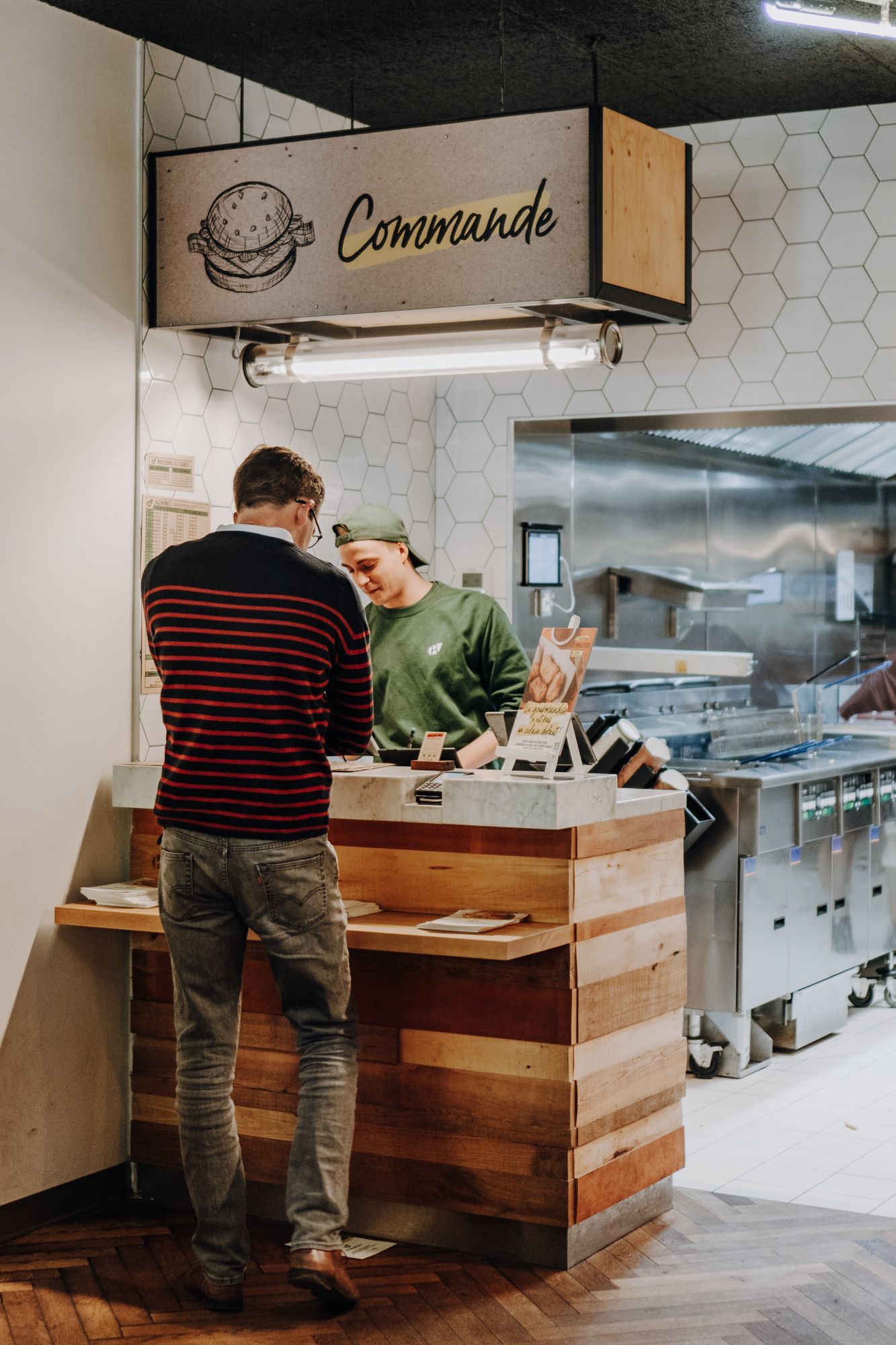 Un comptoir de commande où un client interactionne avec le personnel, proposant des burgers bio, vegan et végétariens.