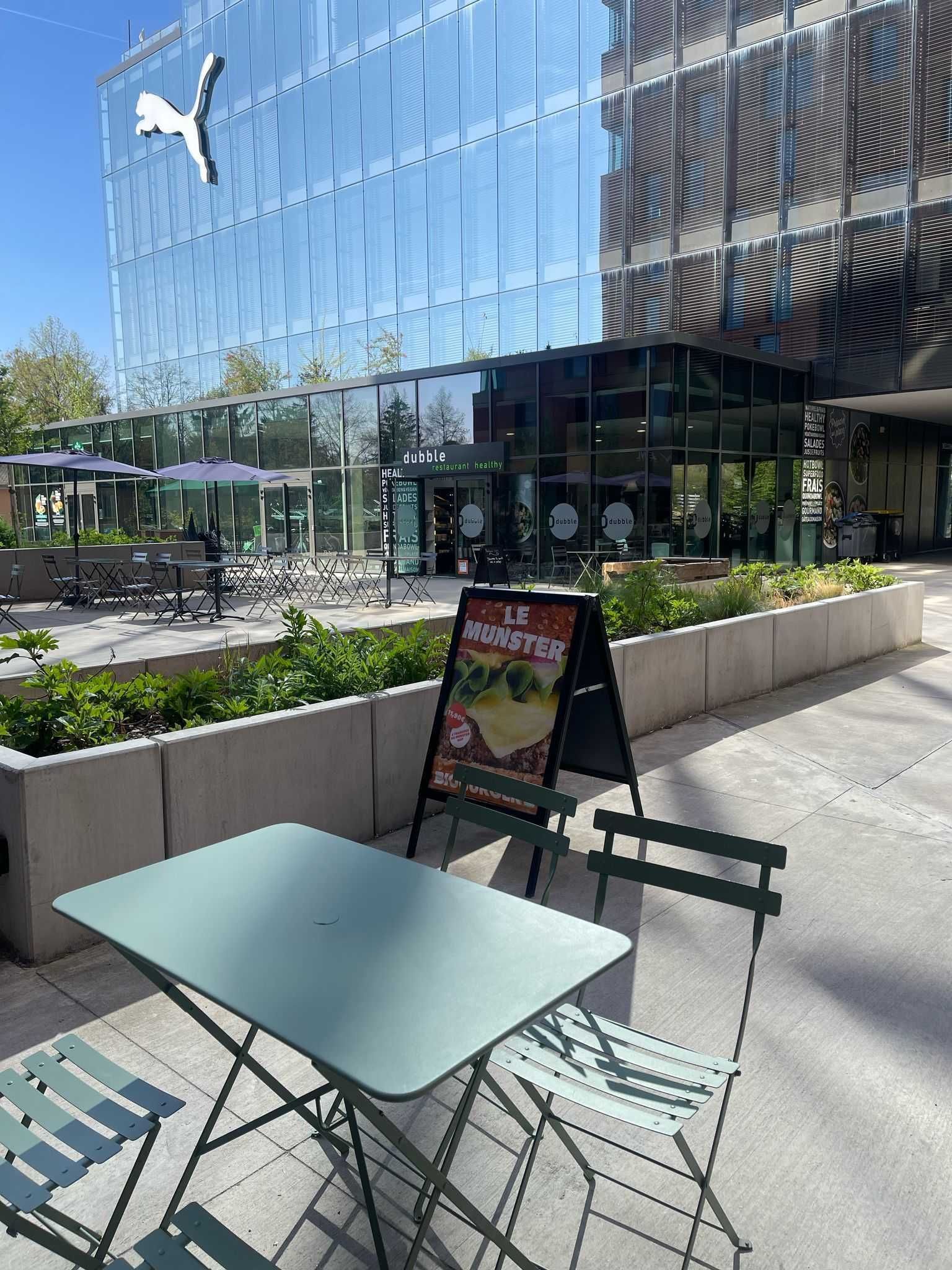Terrasse avec table et chaises, panneau affichant un burger. Établissement moderne en arrière-plan.