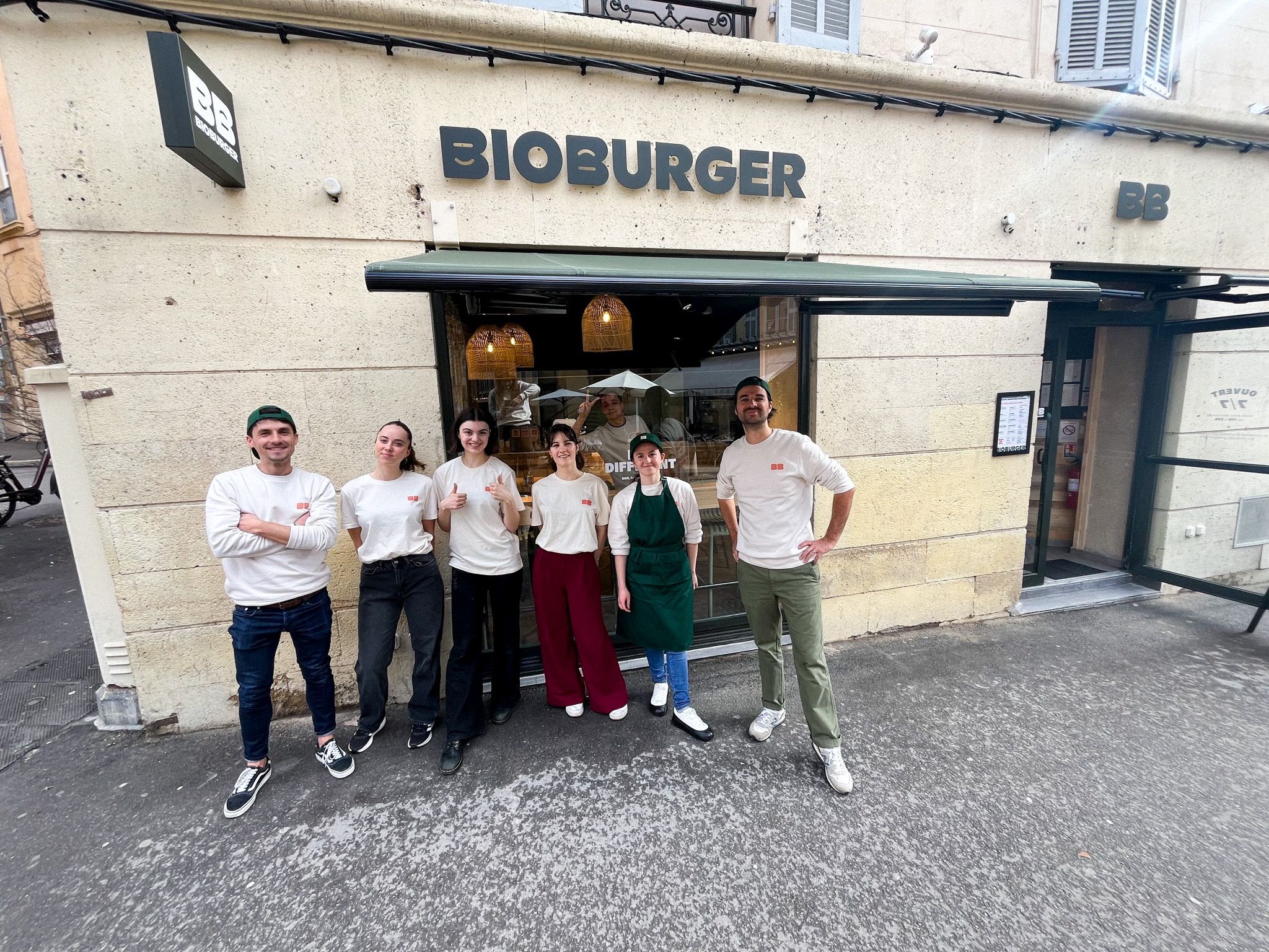 Équipe souriante devant le restaurant Bioburger, spécialisé dans des burgers bio, végétariens et véganes.