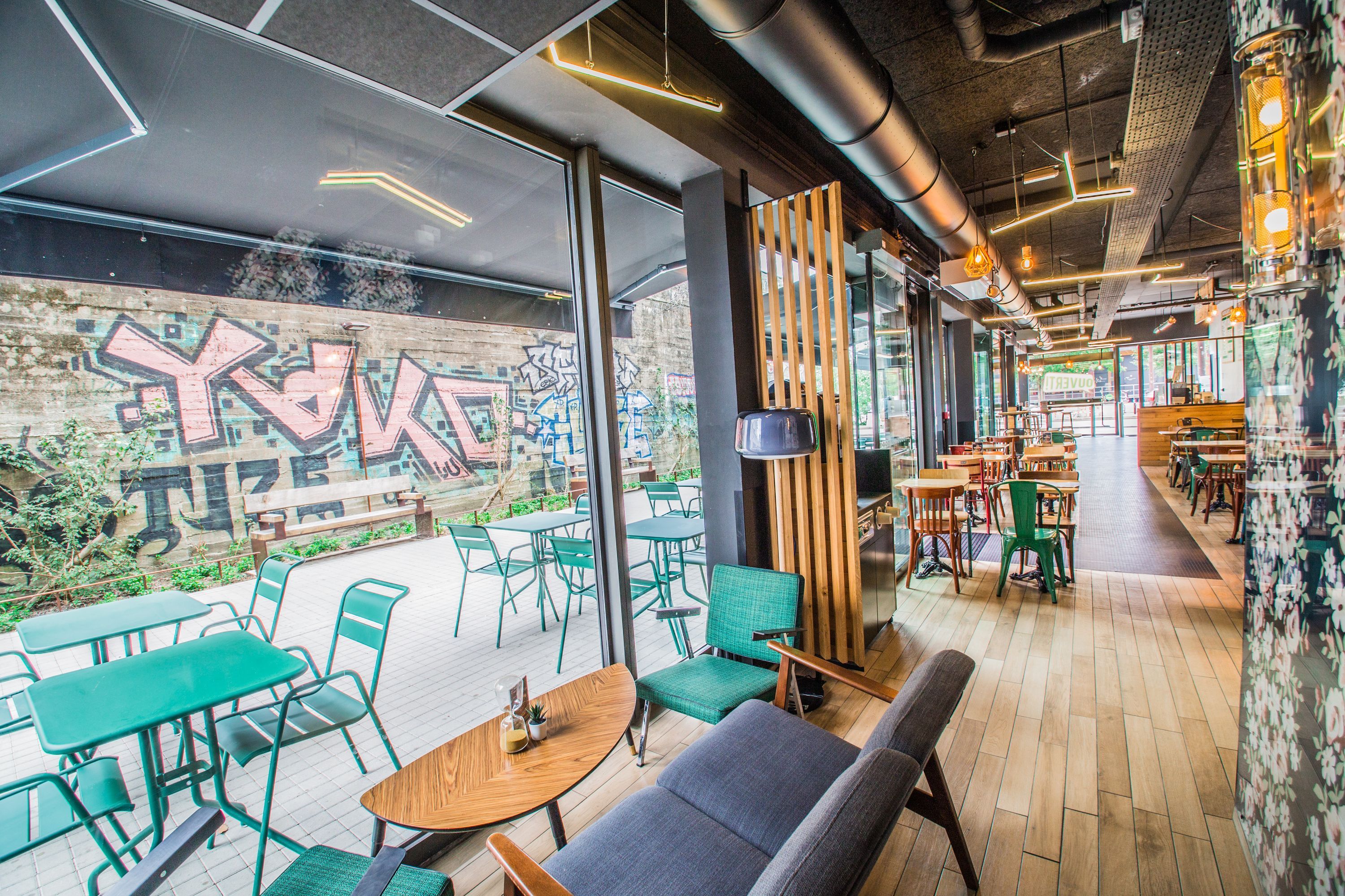 Espace intérieur du restaurant avec des tables vertes, un sol en bois et une décoration urbaine.