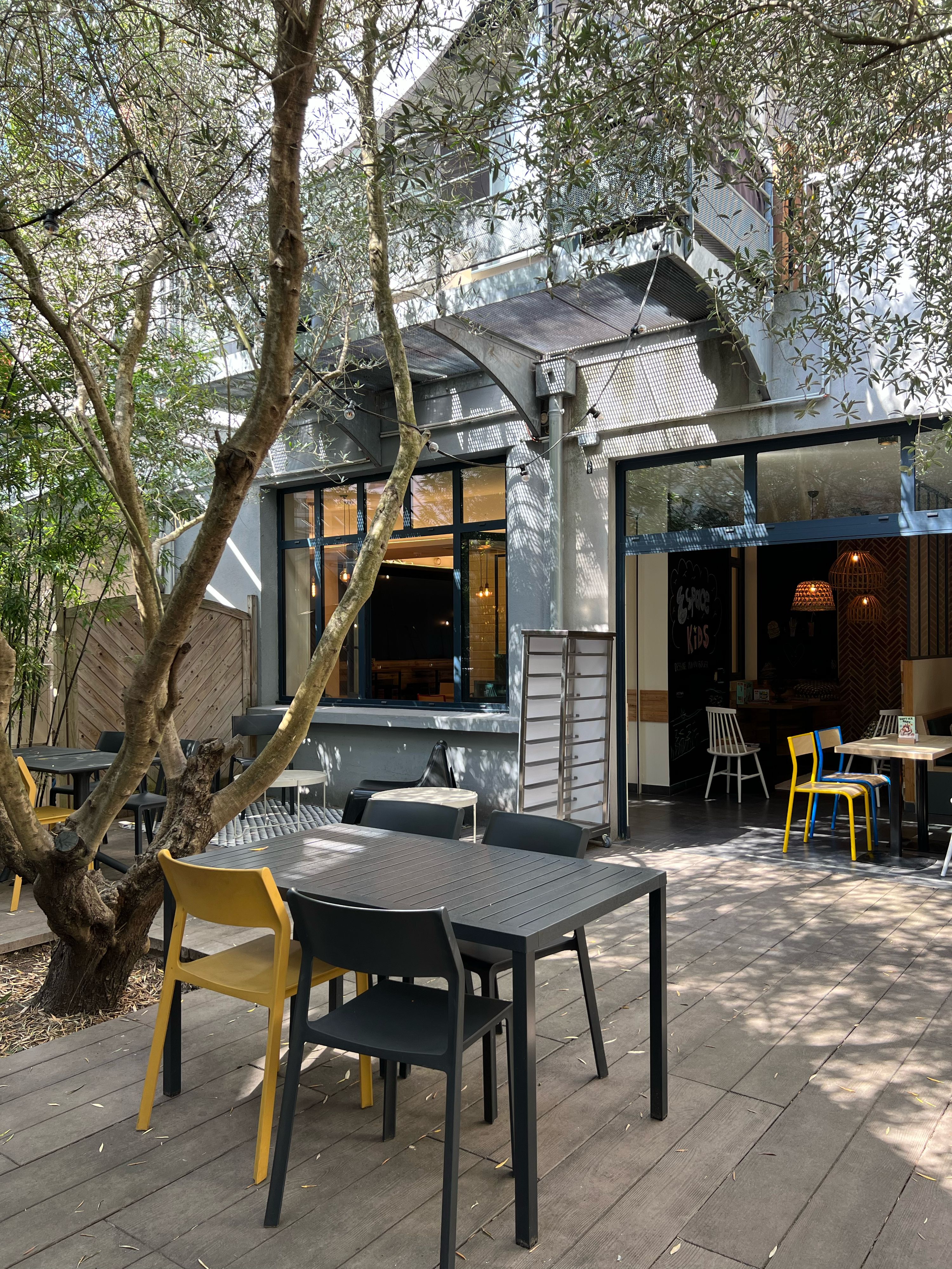 Terrasse extérieure avec des tables et chaises, entourée d'arbres, menant à un restaurant.