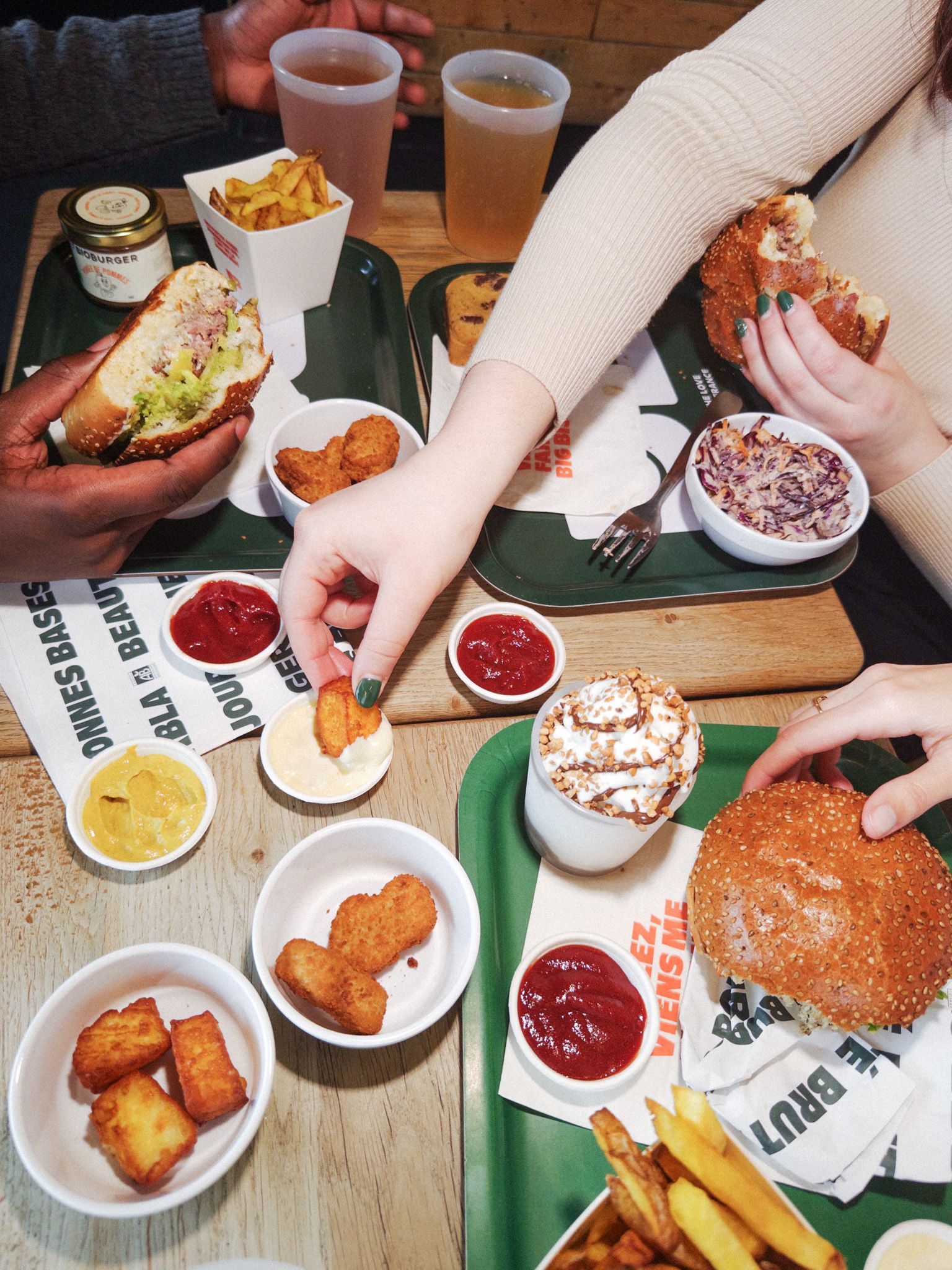 Des burgers bio accompagnés de frites, sauces et plats vegan sur une table partagée.