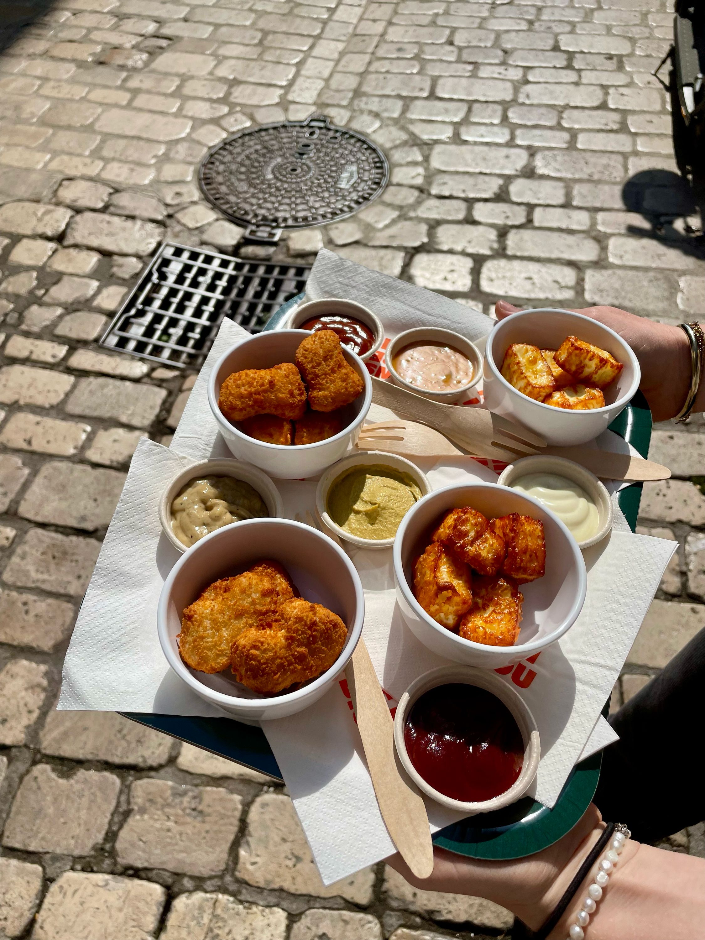 Plateau de nuggets végétariens avec plusieurs sauces, sur une rue pavée.