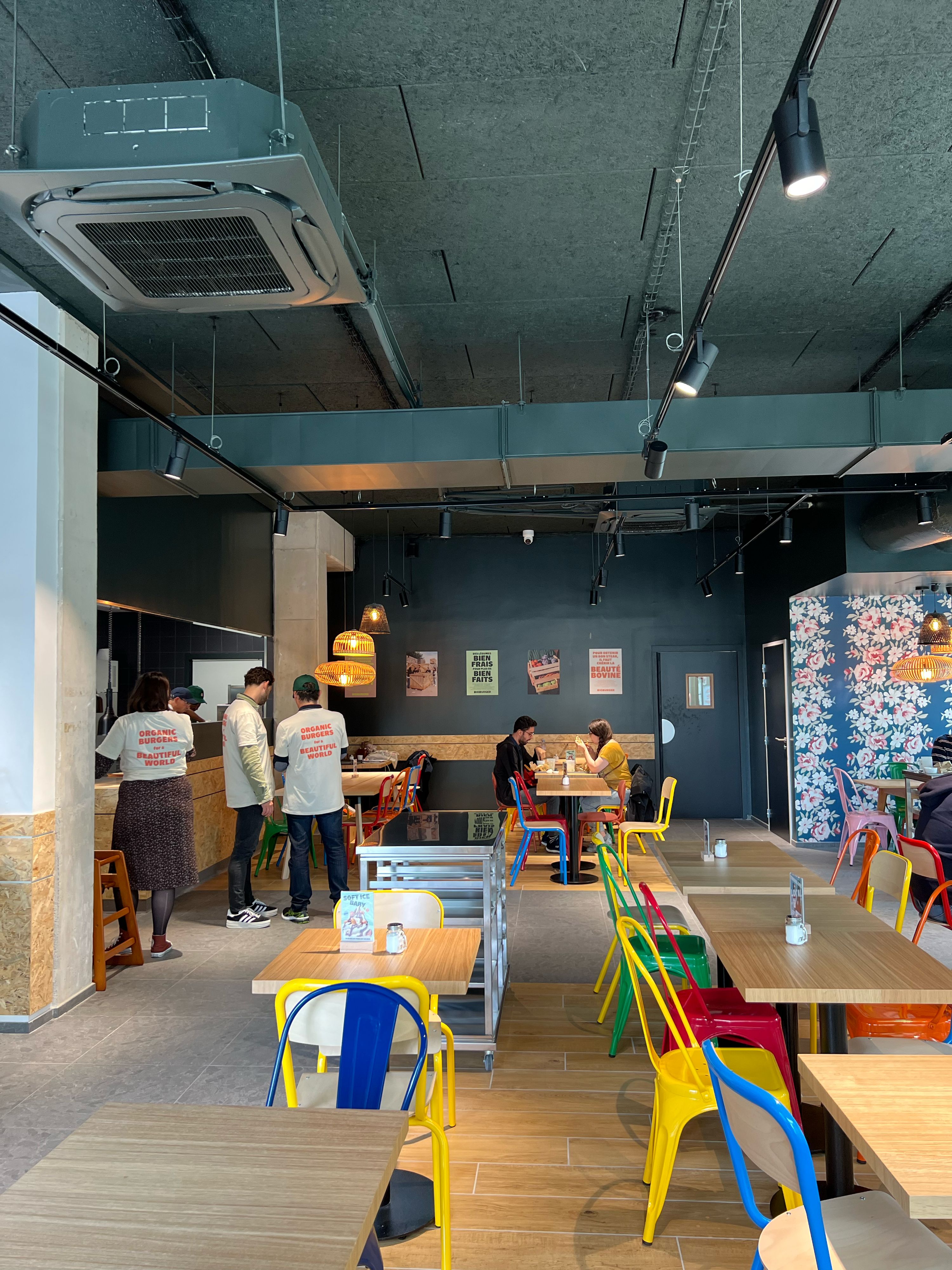 Espace intérieur du restaurant avec des tables colorées et un comptoir en cuisine. Ambiance moderne.
