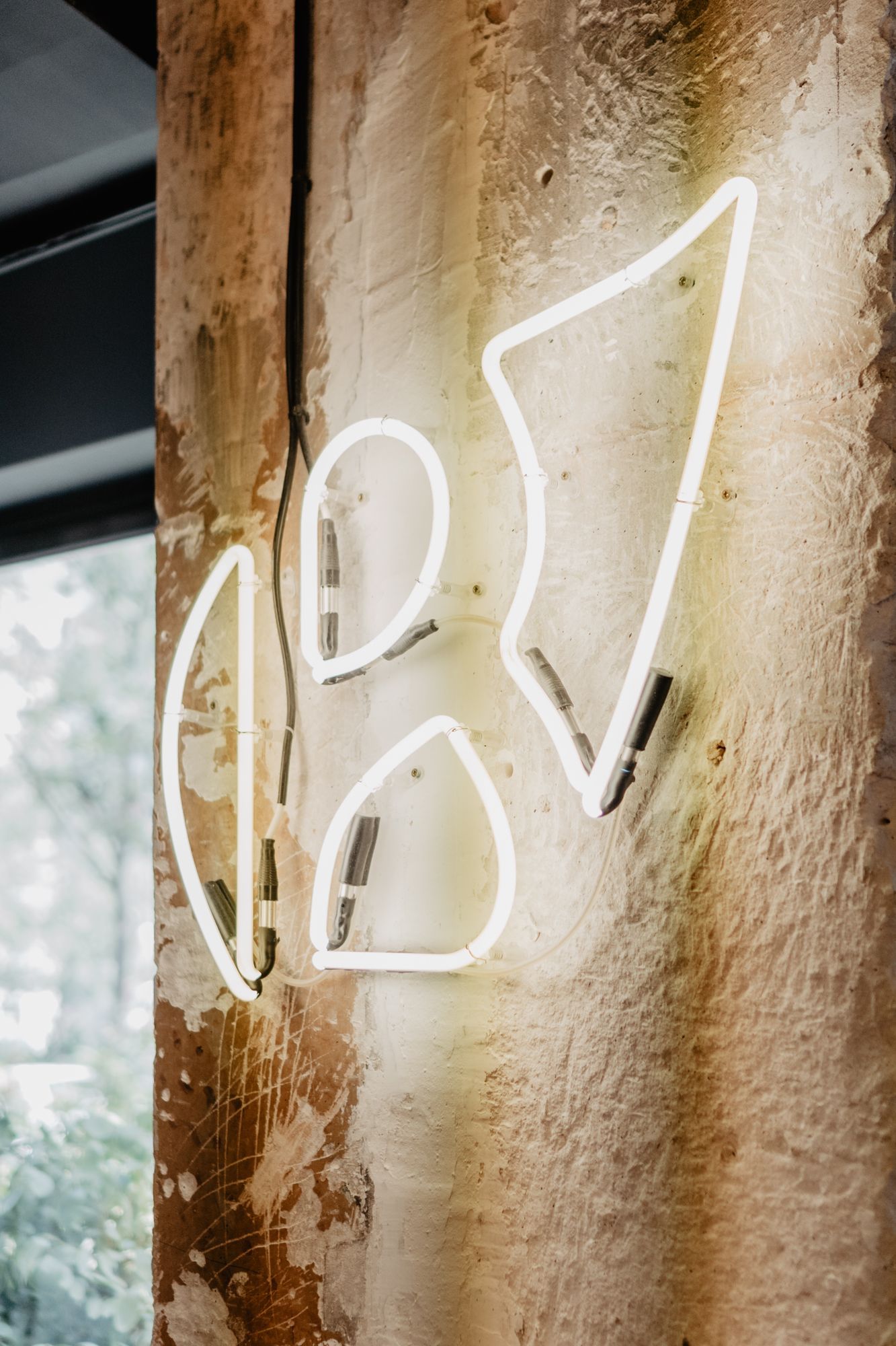 Enseigne néon au design abstrait sur un mur texturé, évoquant un espace unique pour déguster des plats bio.