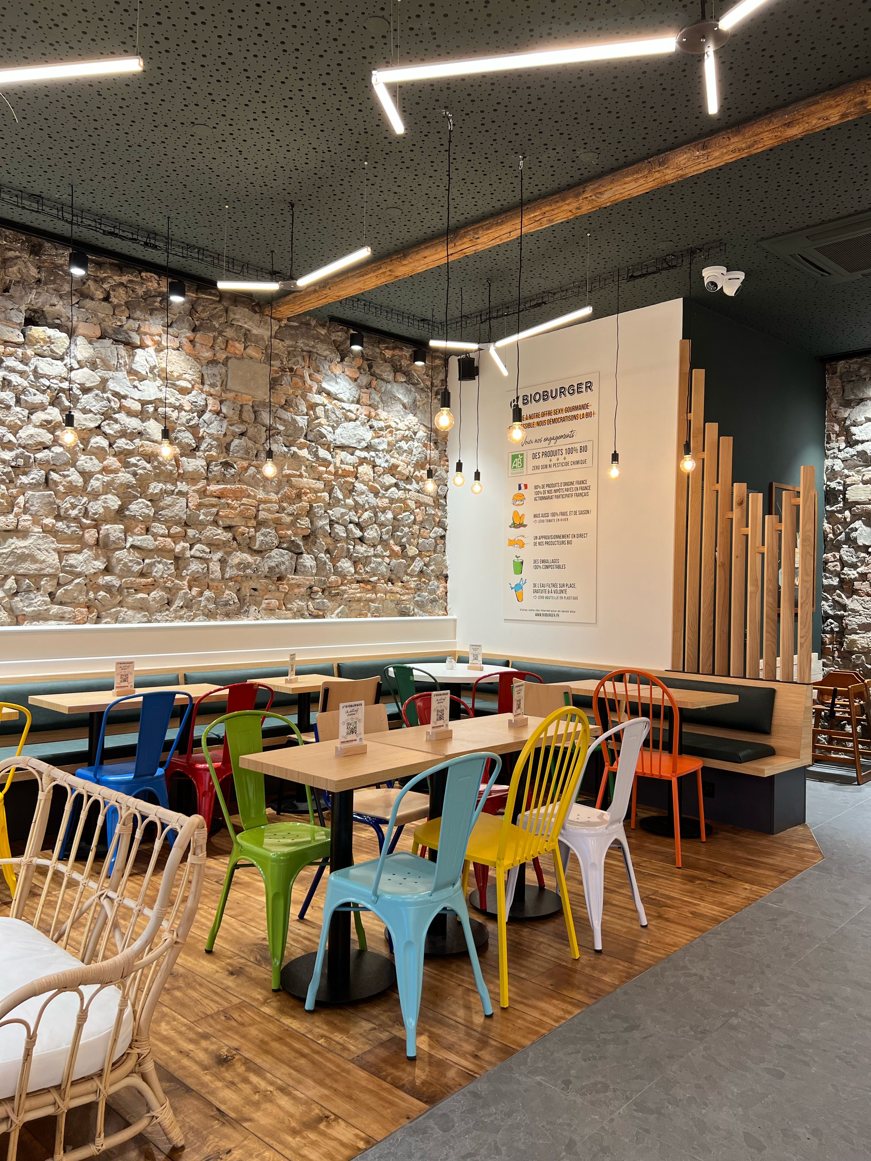 Ambiance moderne du restaurant avec des chaises colorées et un mur en pierre. Menu affiché sur le mur.