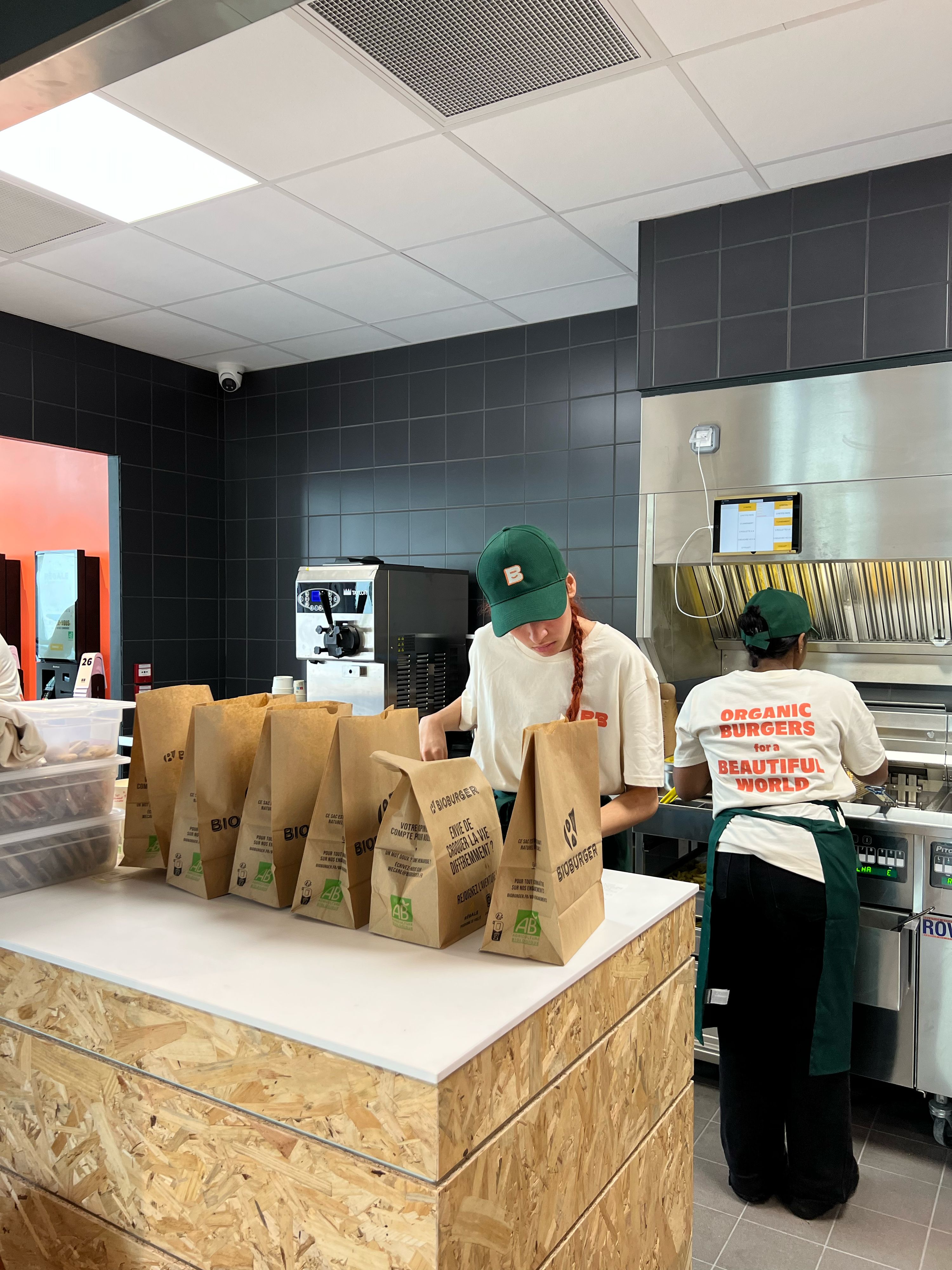 Environnement de cuisine avec des sacs de burgers biologiques et du personnel en action.