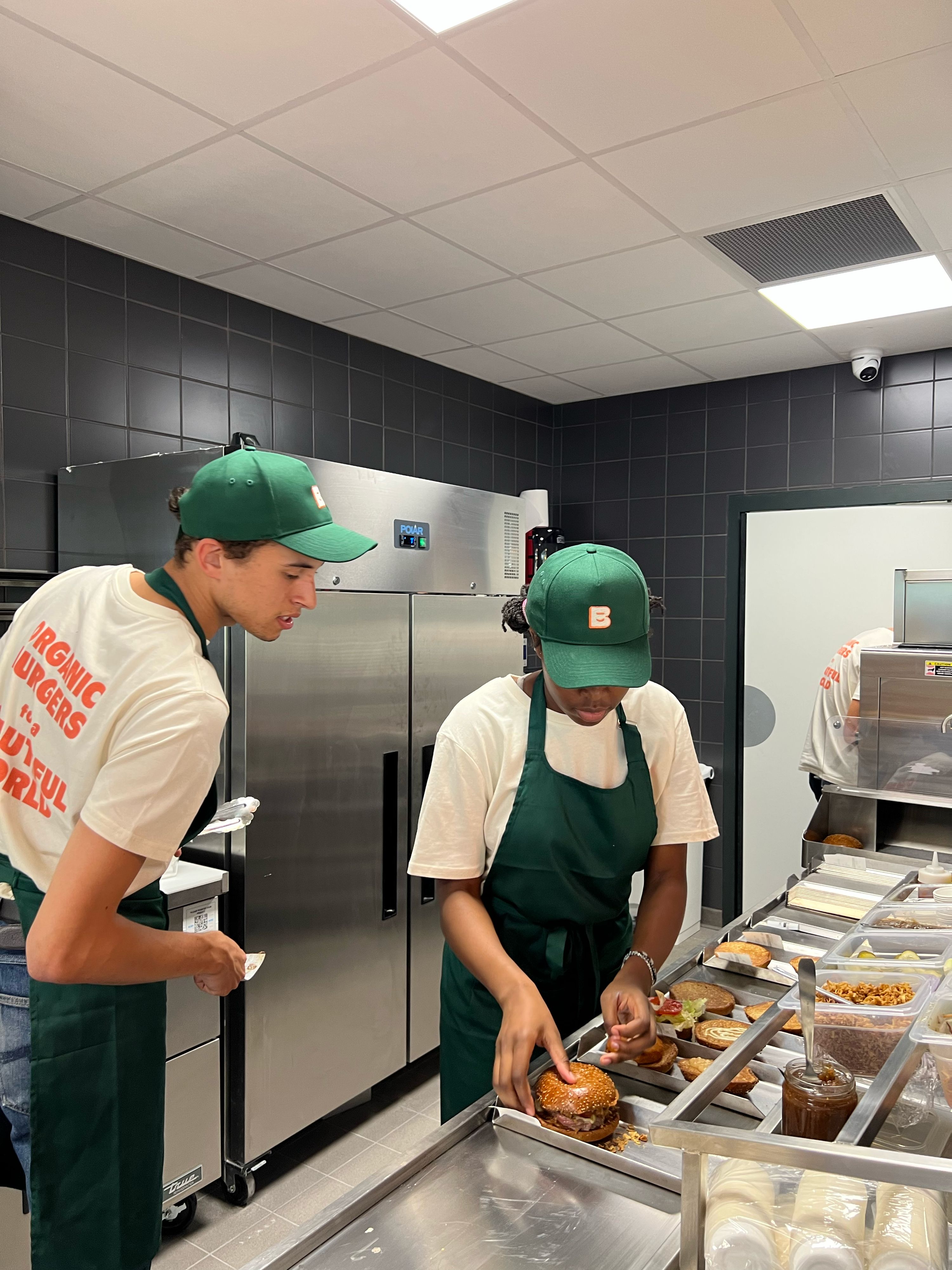 Préparation de burgers bio et végan dans une cuisine moderne, avec des employés en uniforme.