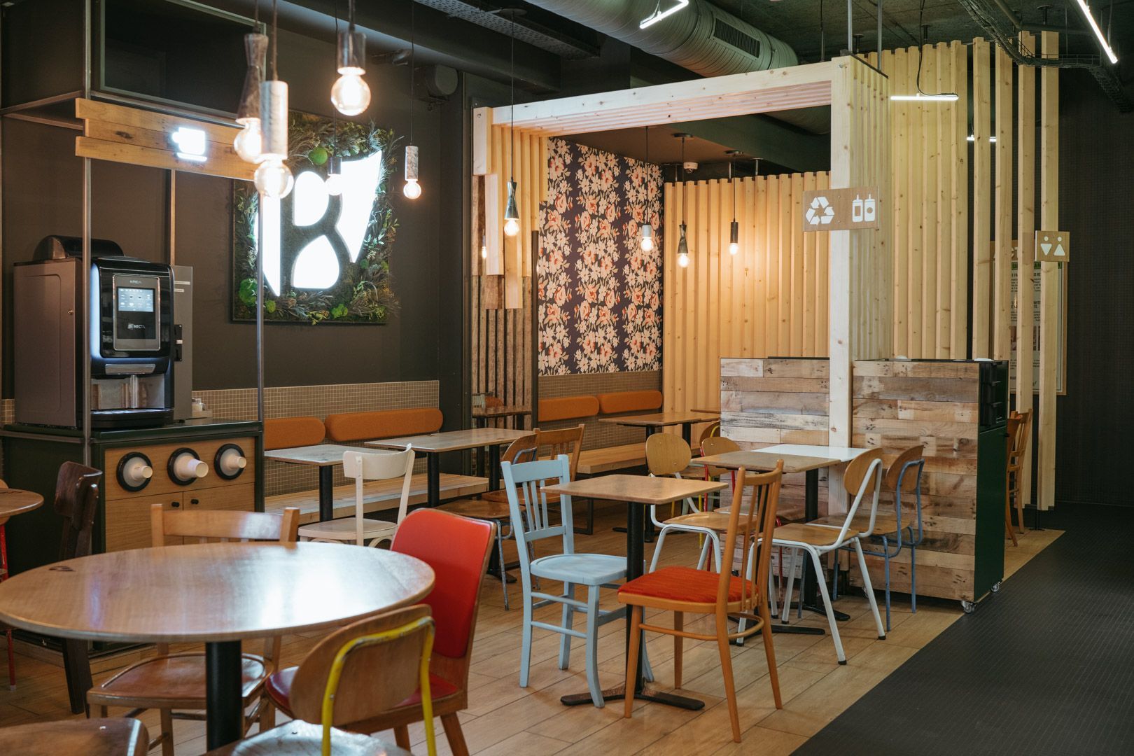 Détail d'un espace intérieur du restaurant avec des tables, chaises colorées et décor en bois.