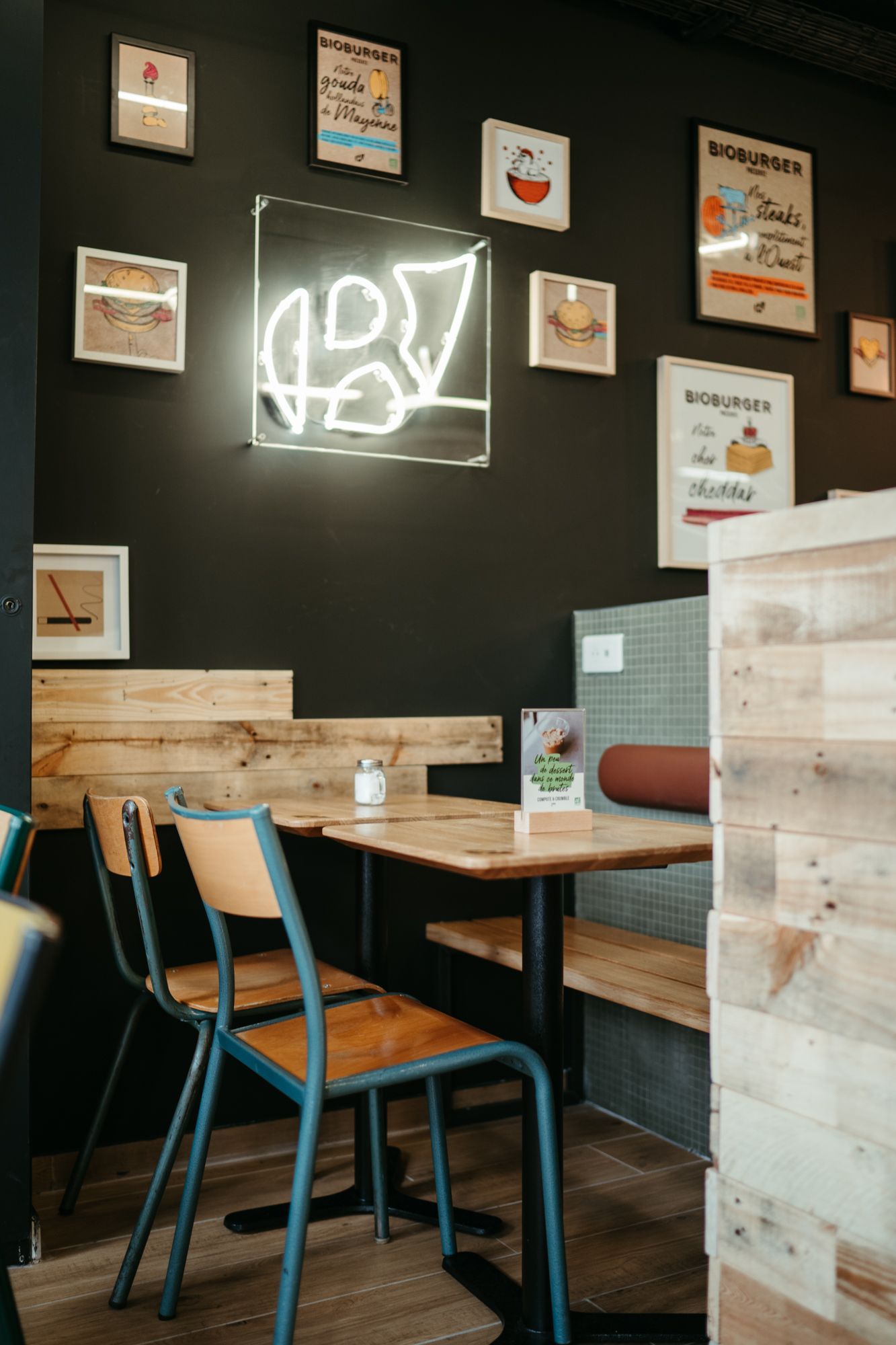 Coin repas avec des chaises en bois et un éclairage néon. Décor mural artistique au restaurant Bioburger Le Marais.