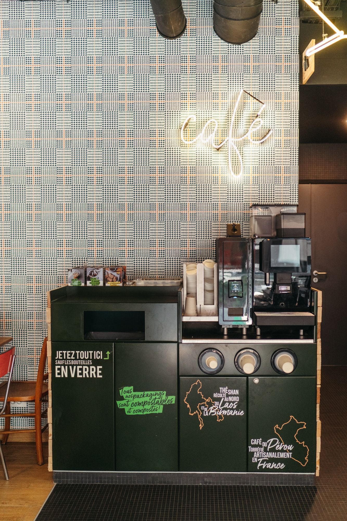 Espace café avec machine à café, comptoir et affiches sur le recyclage et l'agriculture locale.