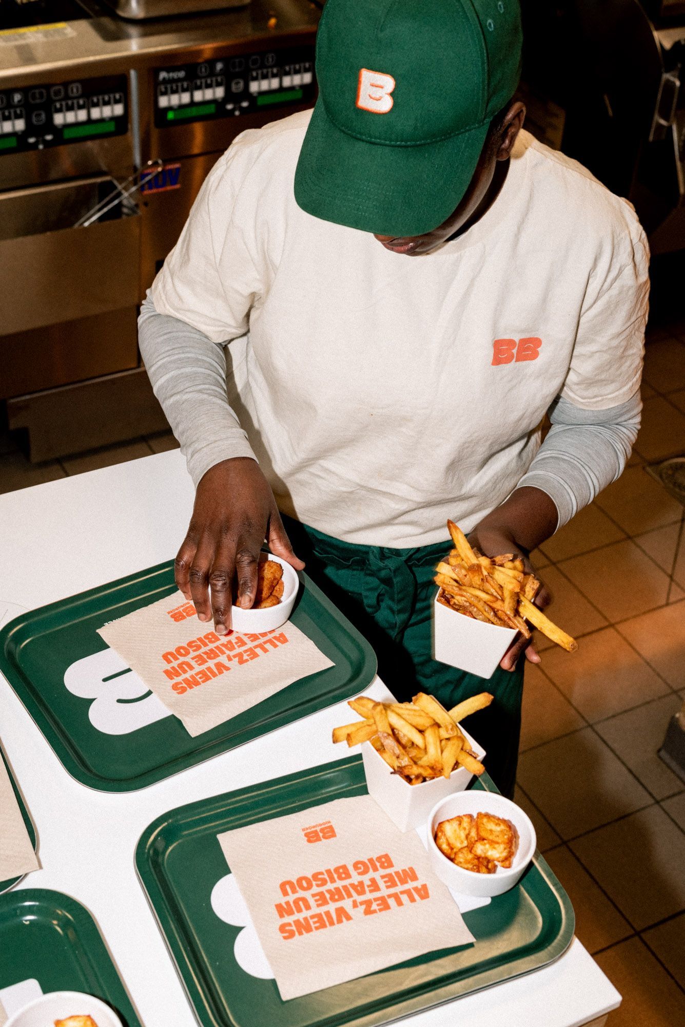 Un employé sert des frites dans un restaurant, avec des plateaux portant le logo Bioburger.