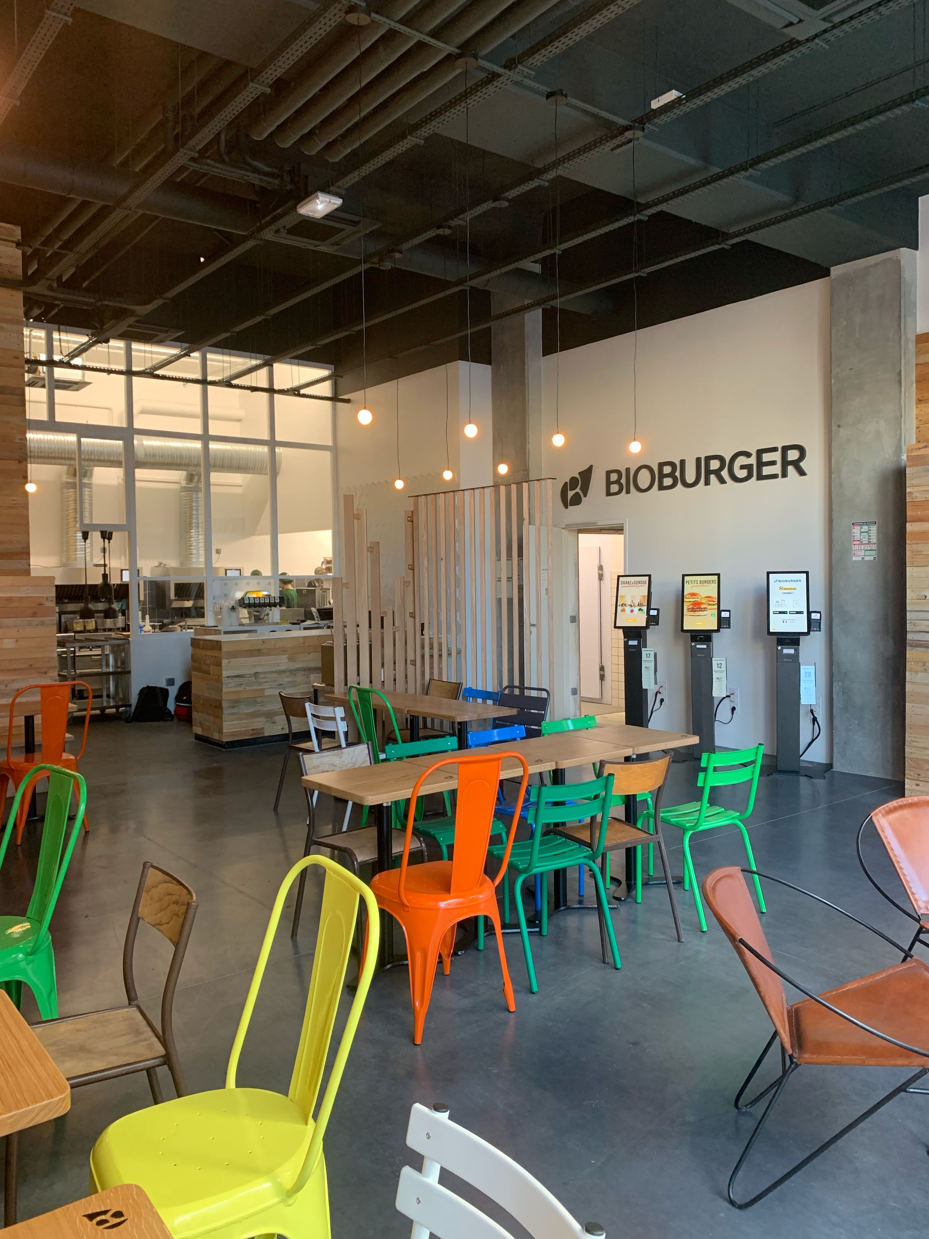 Espace moderne avec tables en bois, chaises colorées et décoration minimaliste. Ambiance décontractée.
