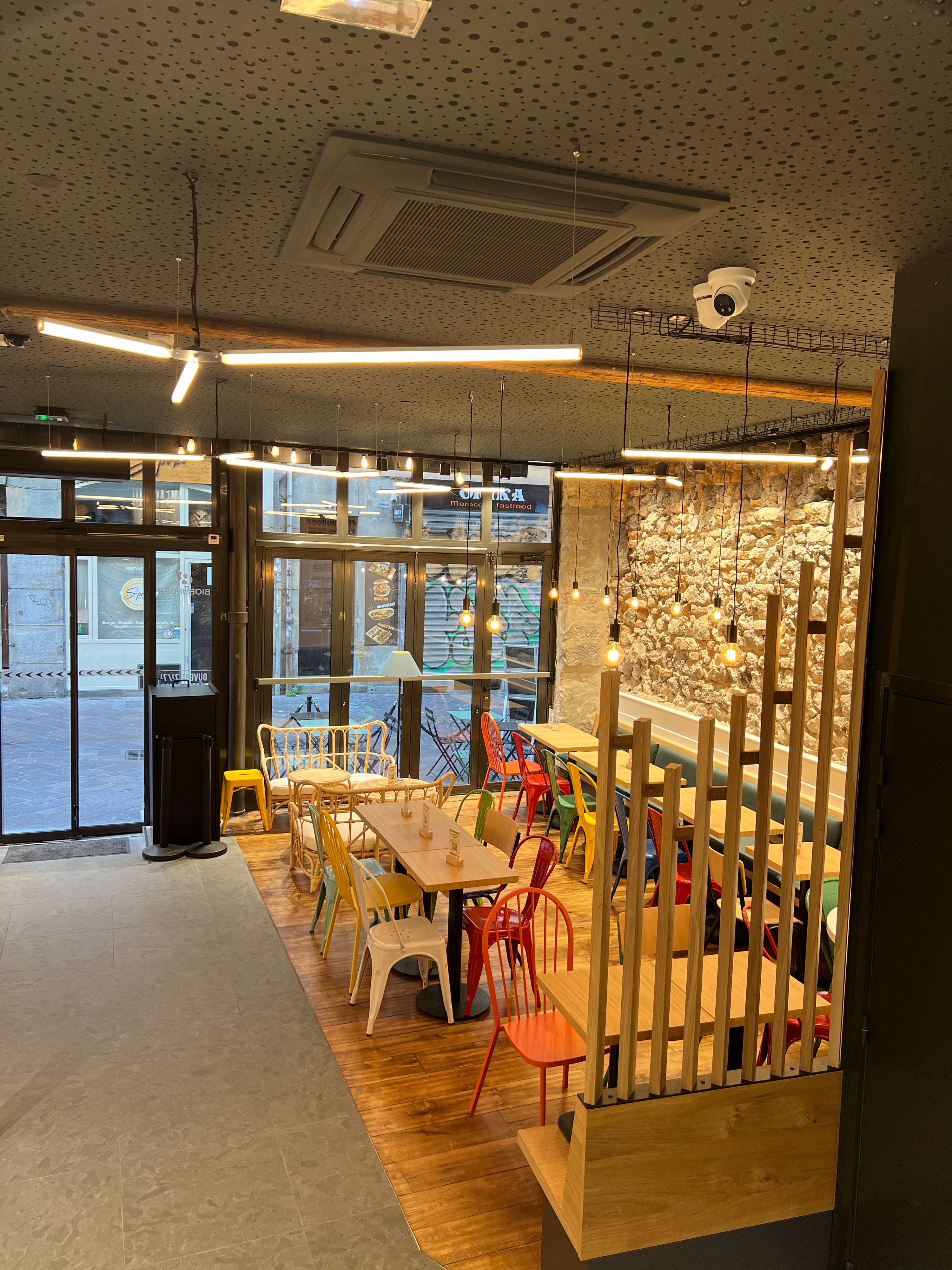 Espace intérieur moderne du restaurant avec tables et chaises colorées, éclairage suspendu et ambiance décontractée.