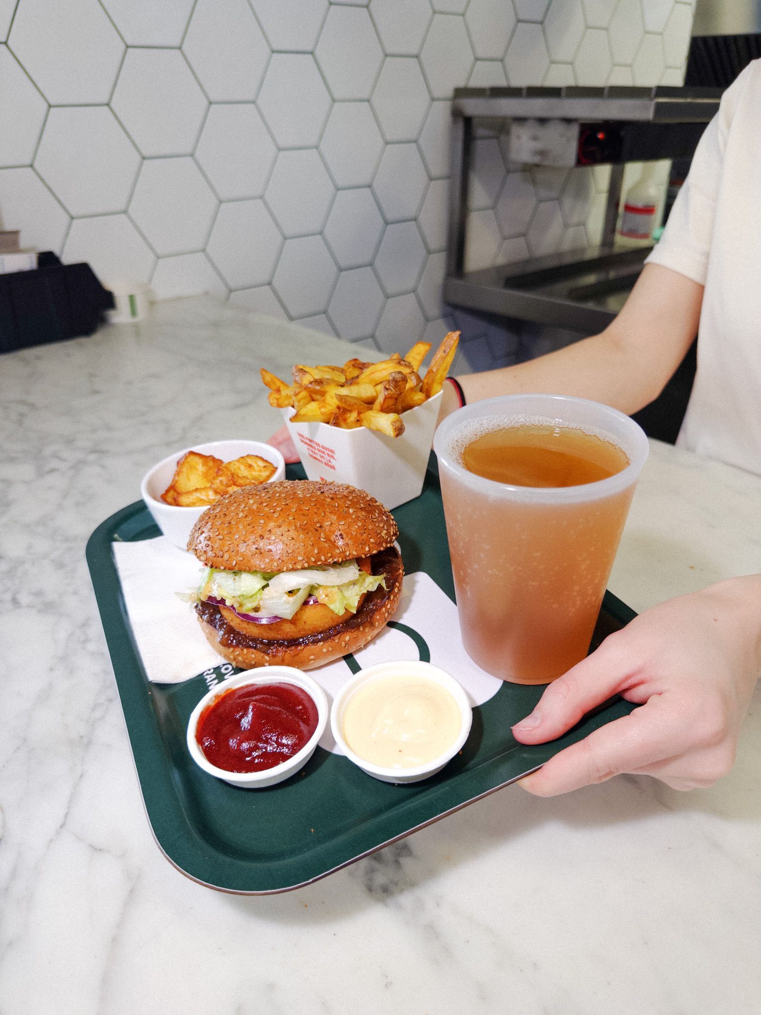 Plateau avec un burger bio, frites, sauces et une boisson dans un restaurant.