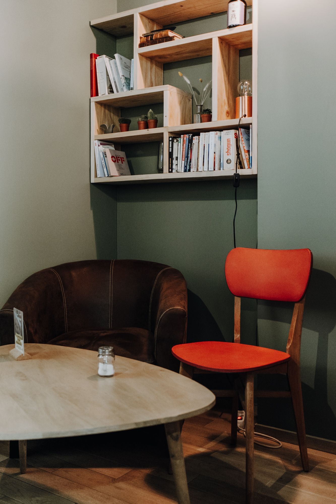 Espace intérieur avec un coin salon, une chaise rouge, une table et des étagères en bois.