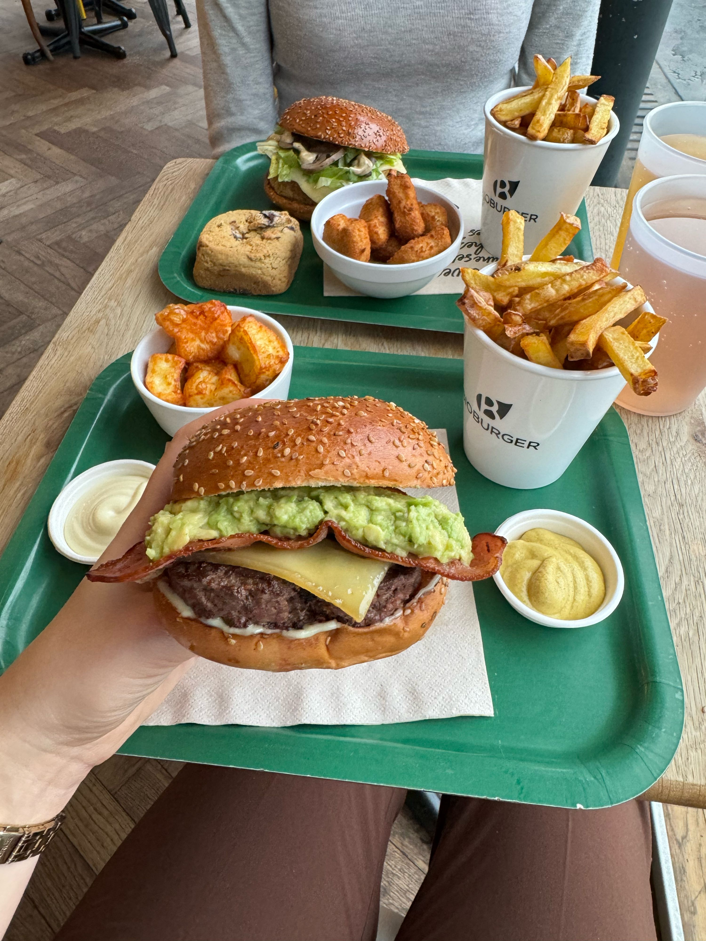 Un burger Bio avec avocat et garnitures, accompagné de frites, bouchées et boisson sur une table.