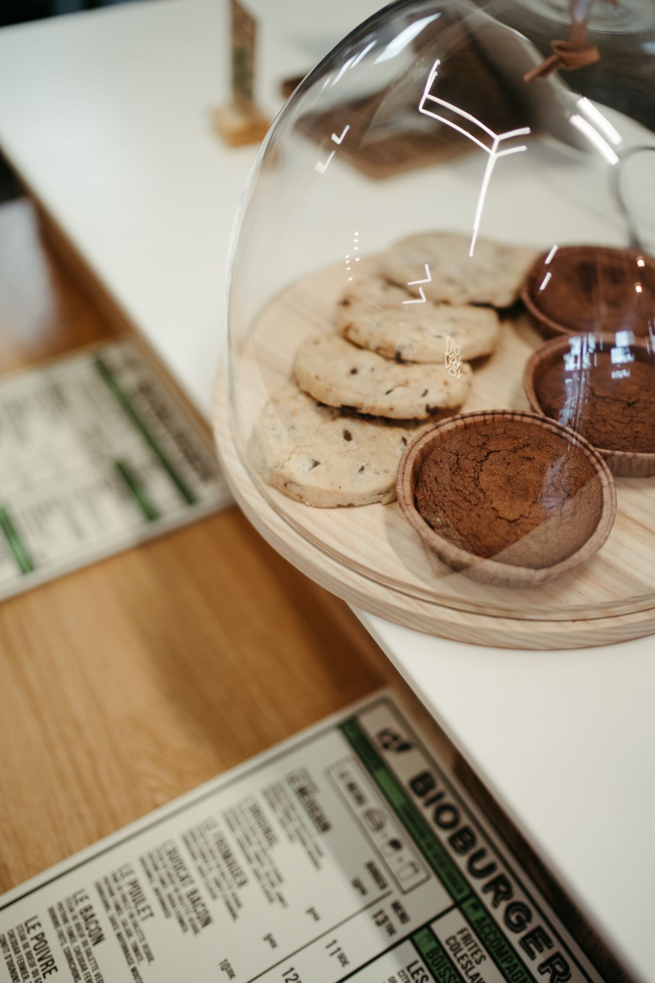Desserts bio exposés sous cloche, incluant cookies et muffins au chocolat, avec un menu bio en arrière-plan.