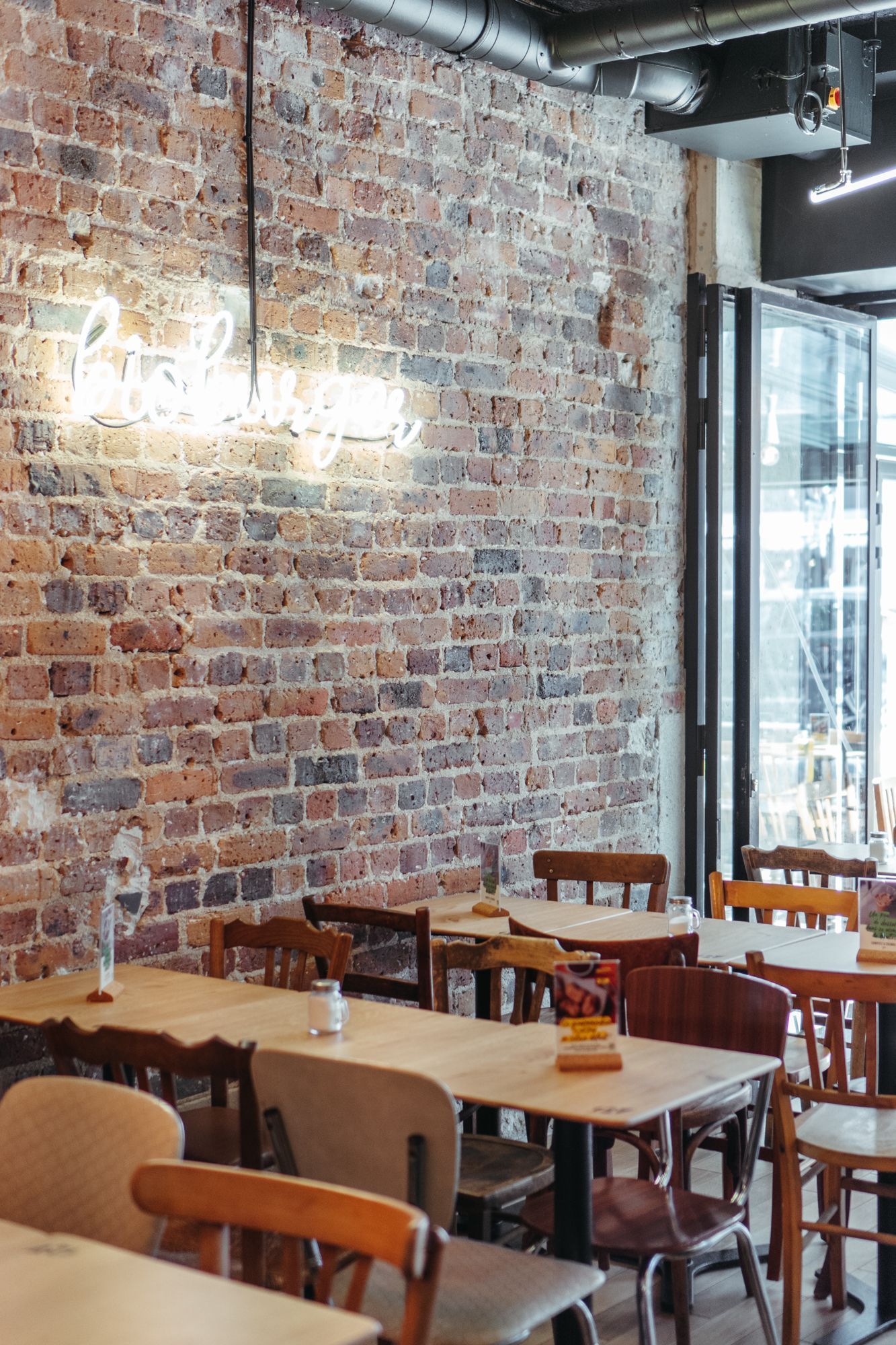 Salle de restaurant avec des murs en briques, tables en bois, ambiance décontractée.