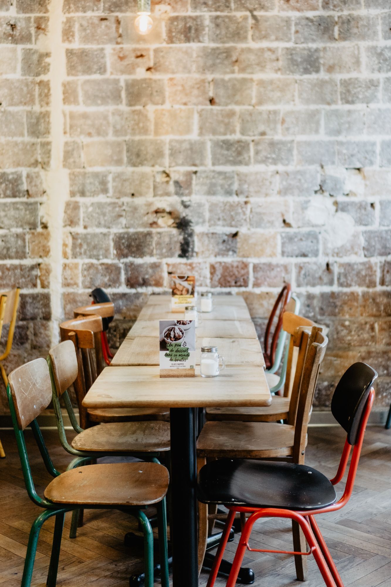 Ambiance d'un restaurant avec des chaises colorées autour d'une table en bois sur un mur en briques.