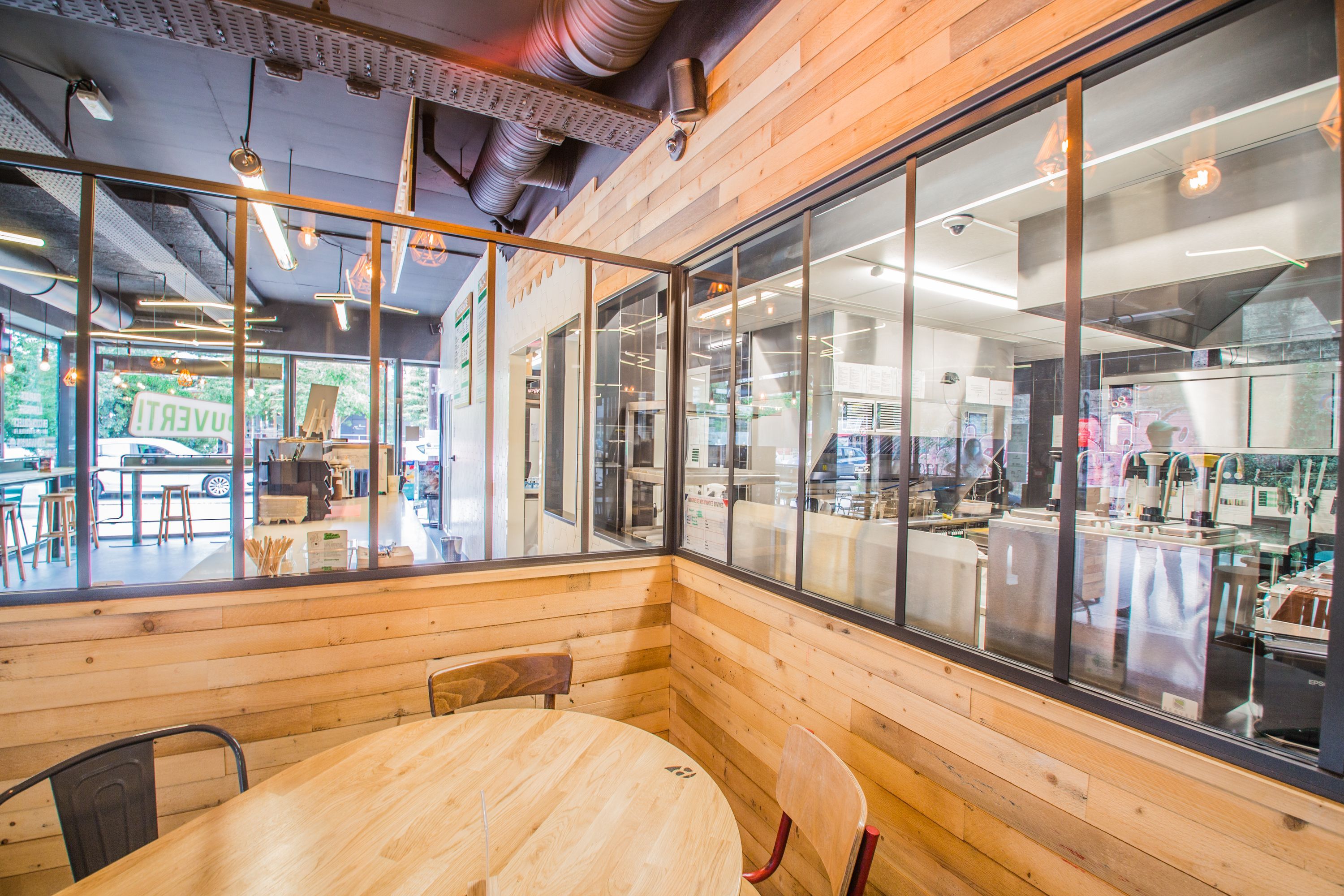 Espace intérieur du restaurant avec un design en bois, tables et fenêtres en verre, ambiance moderne.