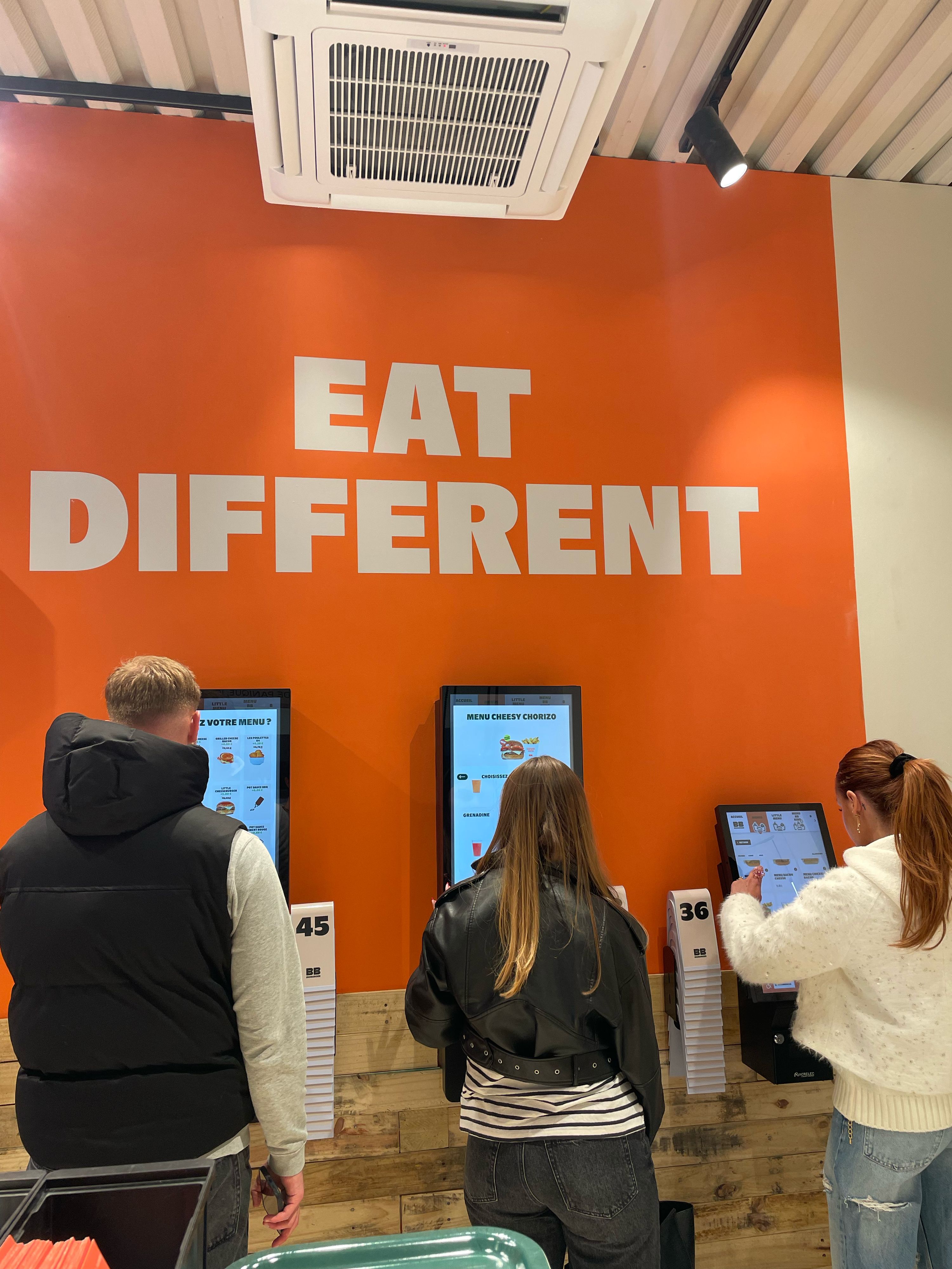 Clients consultant les bornes de commande pour choisir des burgers bio, vegan et végétariens.