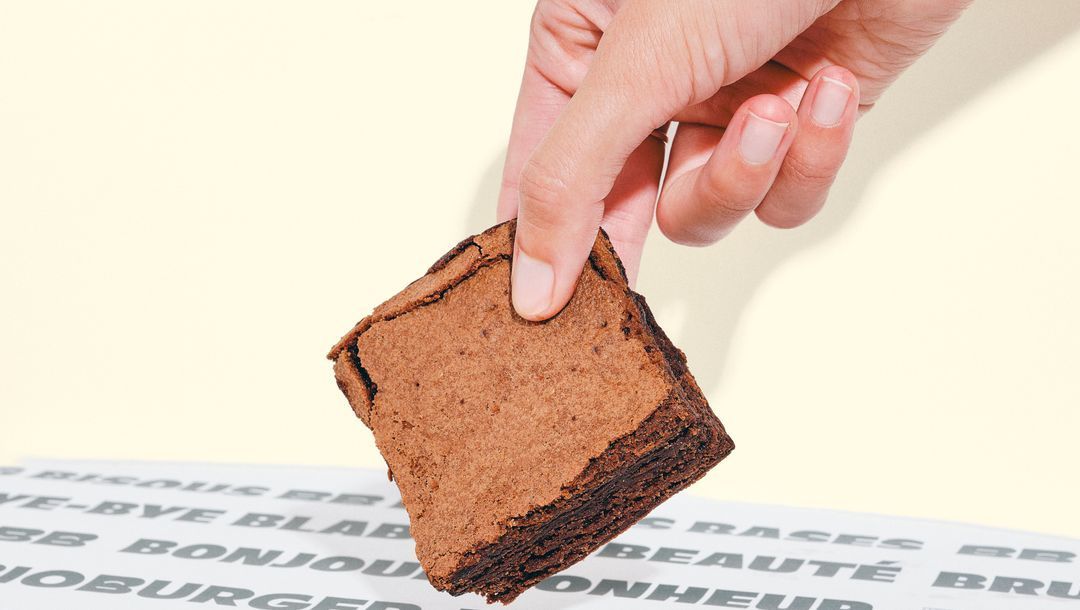 Brownie au chocolat pris par une main, sur une table avec une nappe élégante.