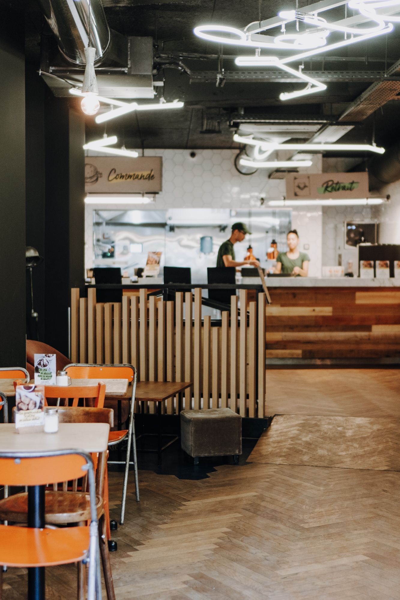 Espace intérieur du restaurant Bioburger Gobelins, avec des tables, des chaises orange et un comptoir visible.