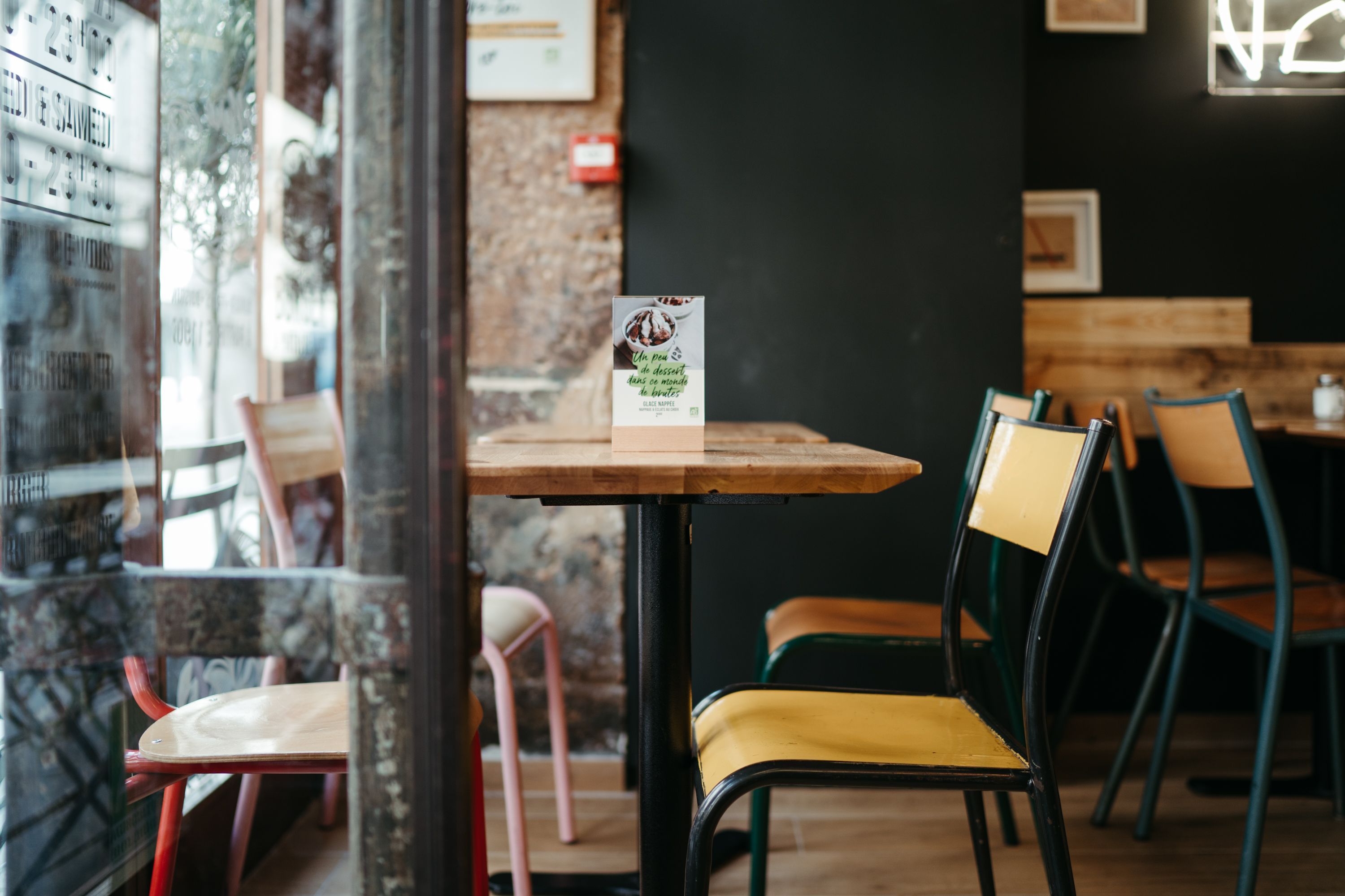 Table en bois avec chaises colorées dans un restaurant servant des burgers bio, végétariens et vegans.